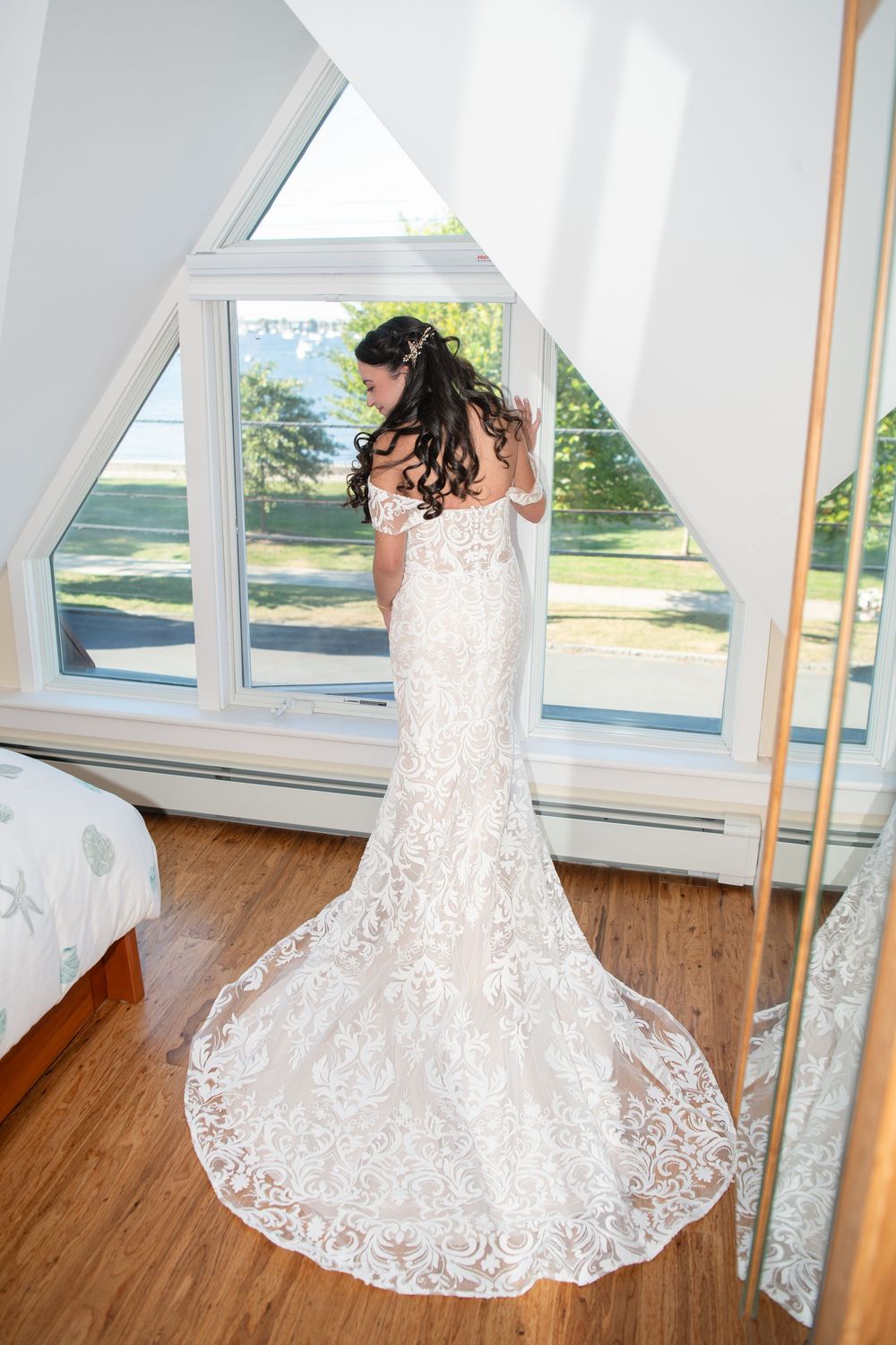 A bride in a white lace wedding dress twirls in a bright room with large windows and wooden floors.