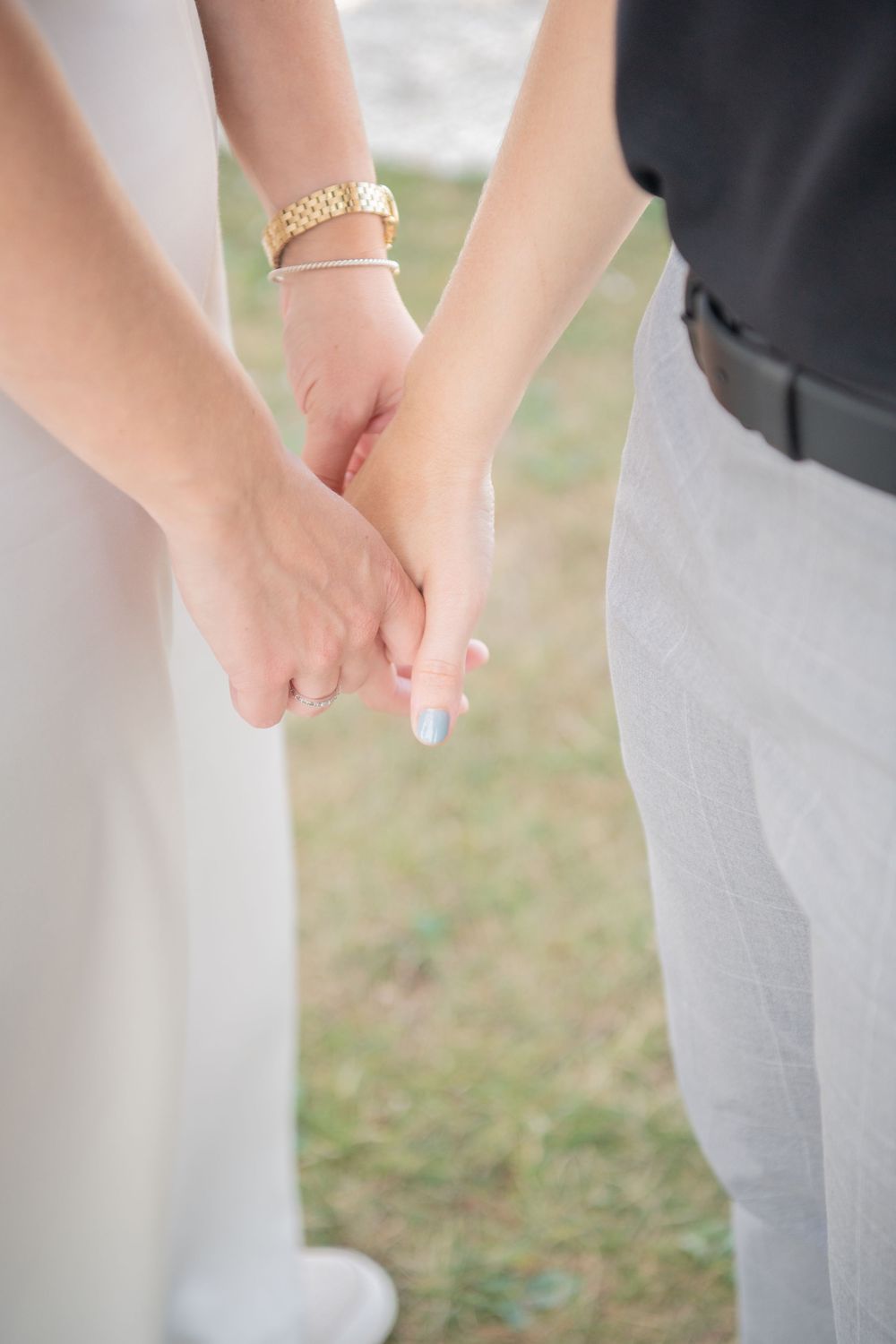 Close-up of a couple holding hands outdoors with the bride wearing a gold bracelet and white dress.