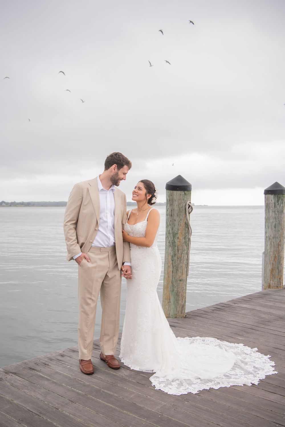 A couple in wedding attire shares a romantic moment on a wooden pier overlooking a misty ocean view.