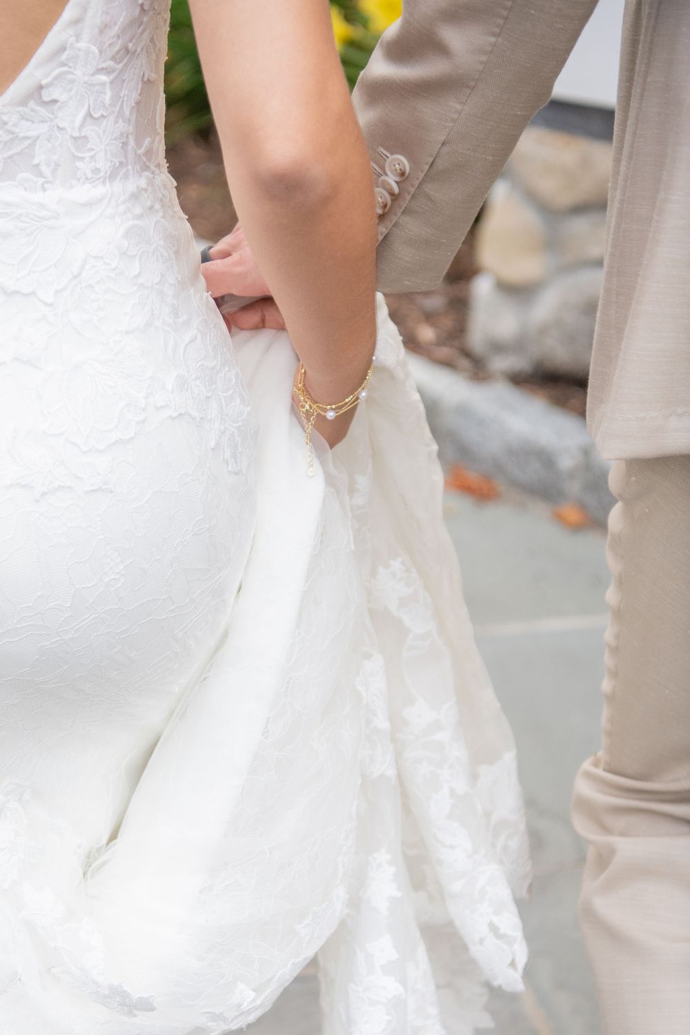 Close-up details of a white lace wedding dress hem being held up while walking outdoors.