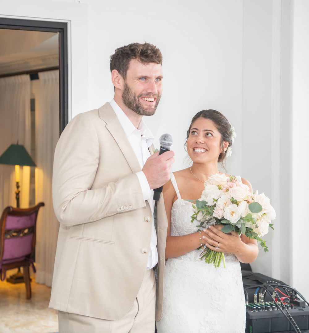 A couple shares a tender moment on their wedding day, wearing cream and white attire with soft peach floral bouquet.
