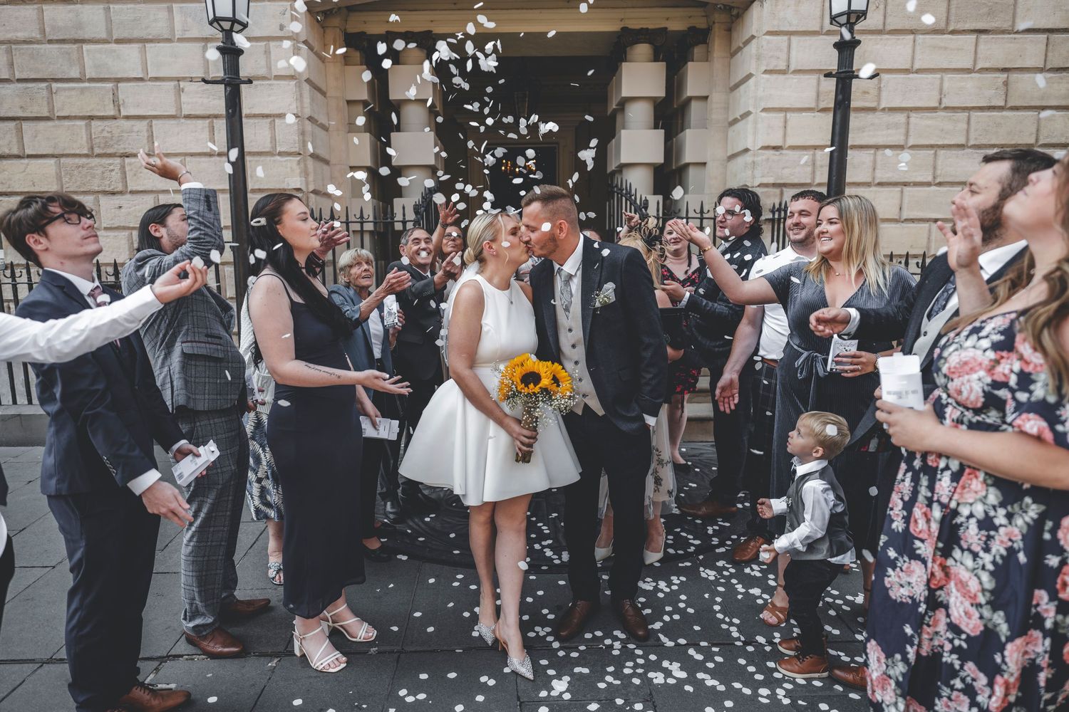 Wedding guests throw confetti over couple during outdoor celebration.