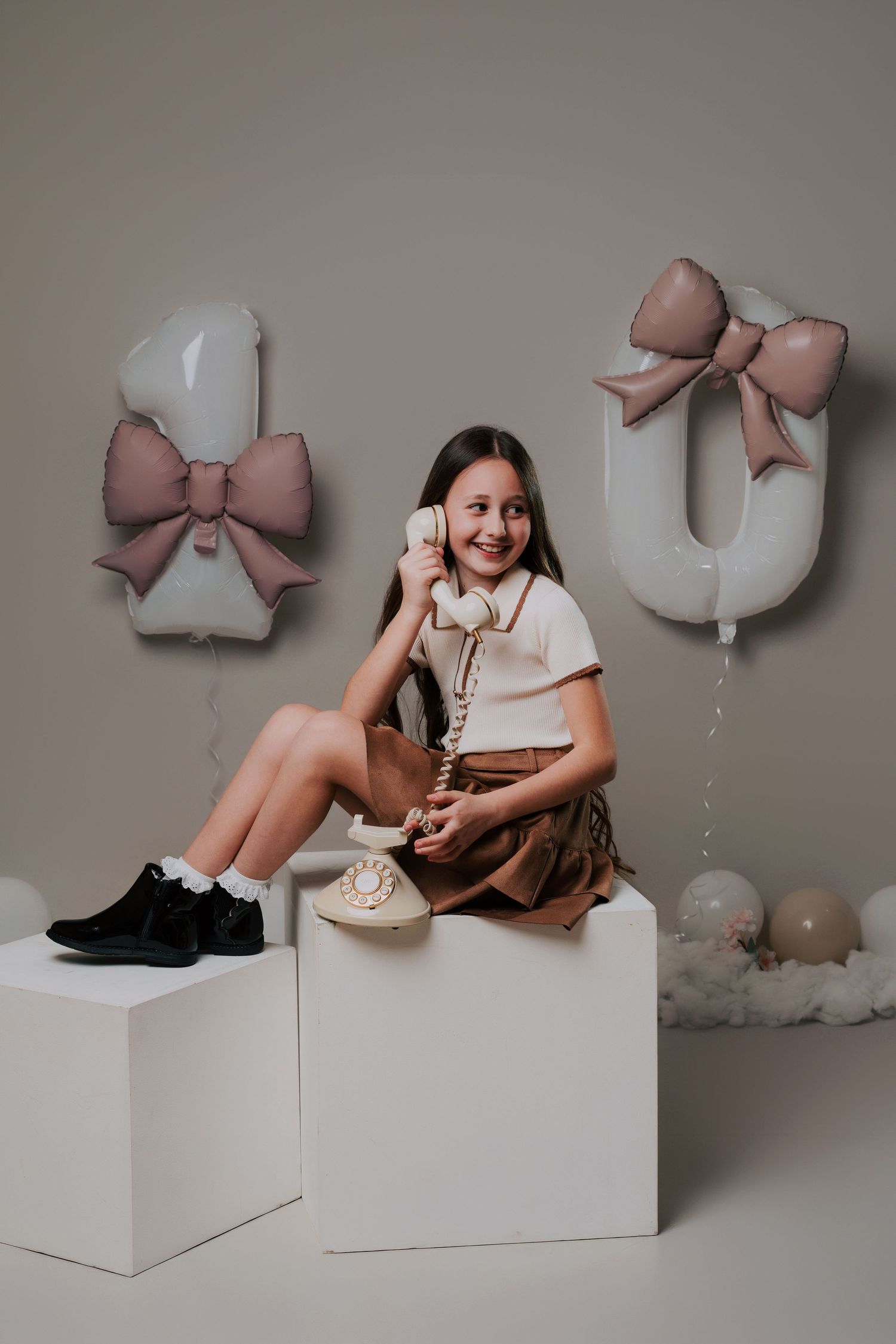 A series of styled photos showing a child sitting on white blocks with decorative bows and soft elements in a studio setting.
