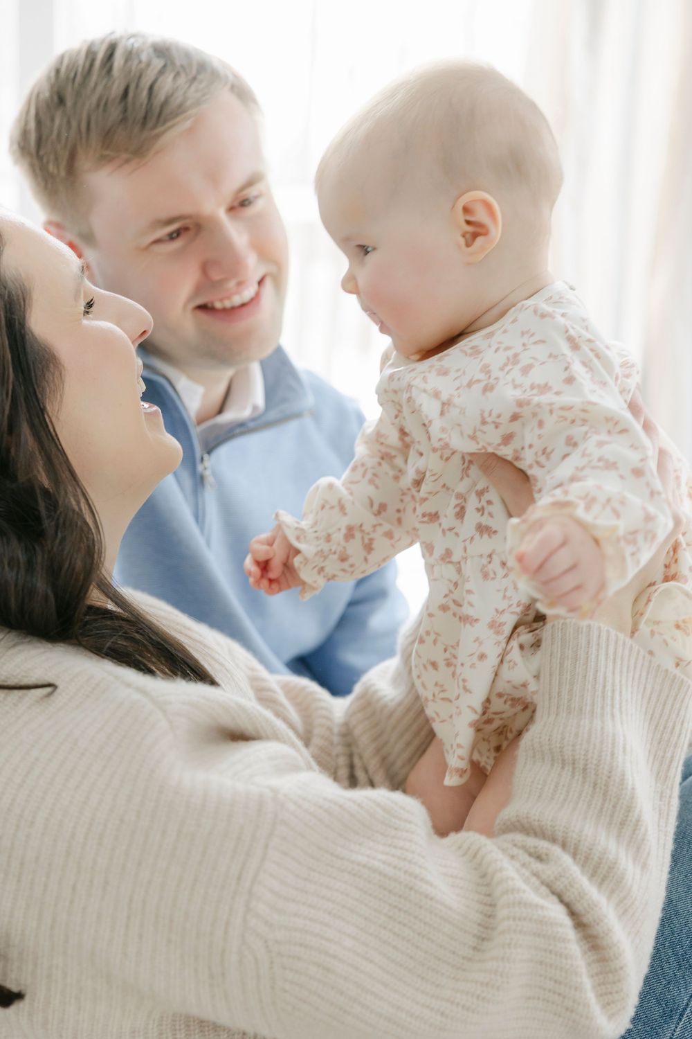 A happy family moment as parents share a tender interaction with their baby wearing a floral onesie.