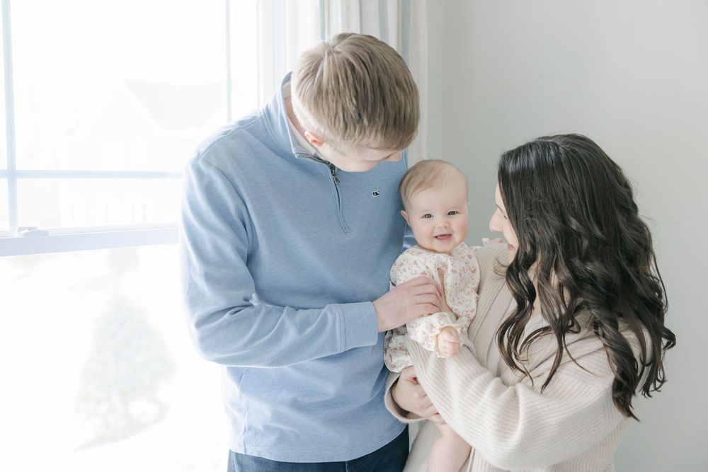 A family wearing light blue and white clothing poses together in a bright room for casual portraits.