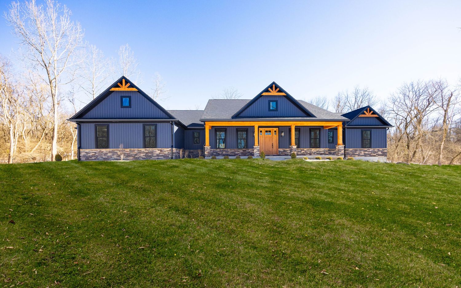 A panoramic view of modern farmhouses with blue roofs nestled on a grassy hillside against a bright sky.