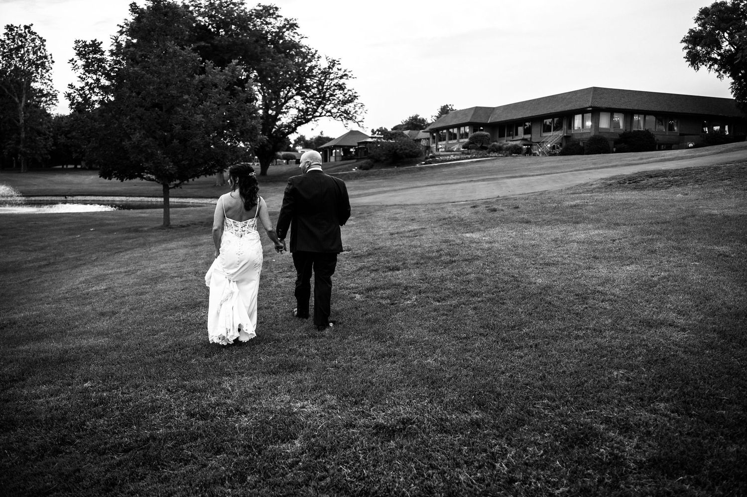 A couple in wedding attire walks together on a grassy path outside a stone building on their special day.