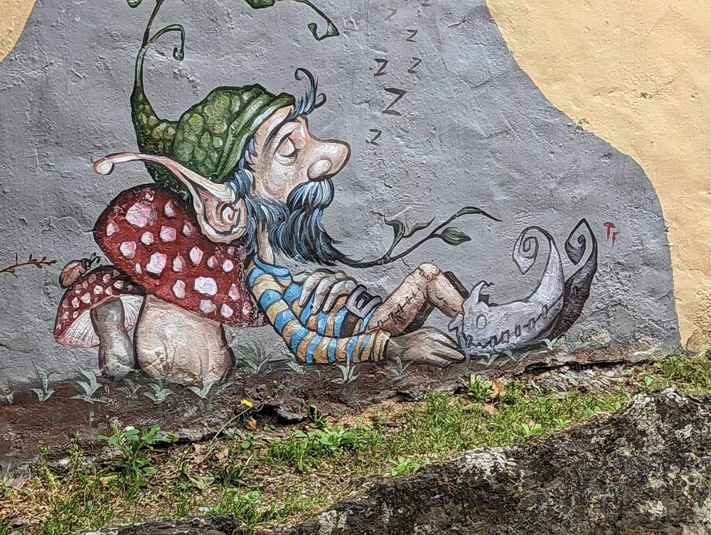 Whimsical street art mural showing cartoon characters lying down painted across a long concrete wall.