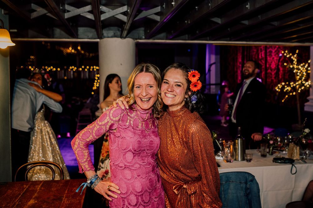 People dancing and celebrating at a lively party with colorful lighting and festive decorations in the background.