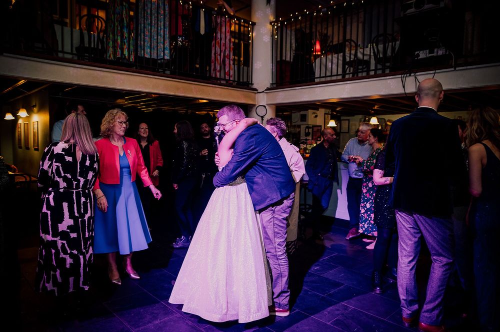 People dancing and mingling at an evening wedding reception with purple and blue lighting.
