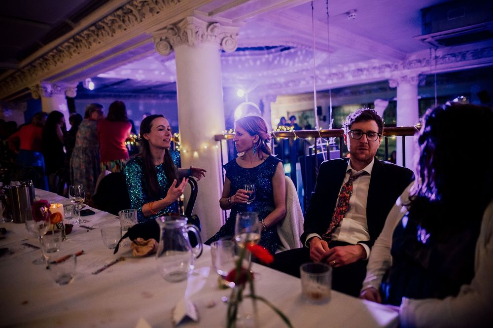 People gathered at a dimly lit indoor venue with purple lighting and columns during an evening event.