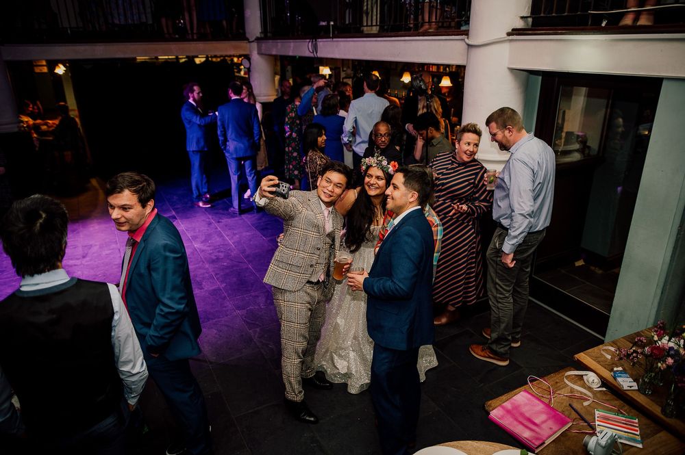 A crowd mingles in a modern indoor space with atmospheric lighting and architectural details.