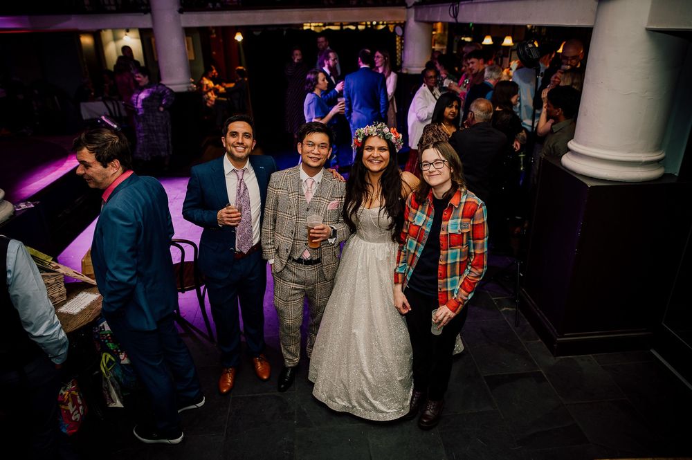 Wedding guests dance and celebrate on a dark dance floor illuminated by purple lighting.