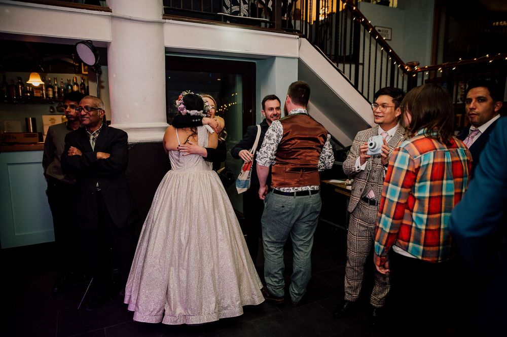 A group of party guests dancing and socializing at an indoor event with a white pillar and staircase visible.