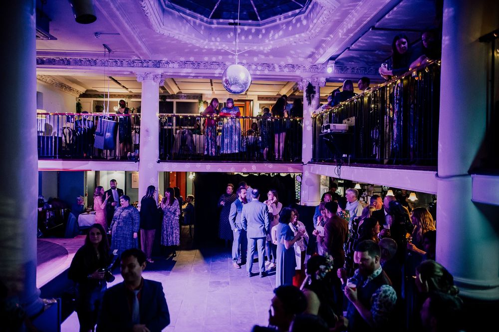 Wedding reception dance floor illuminated in purple lighting with guests dancing and celebrating at an indoor venue.