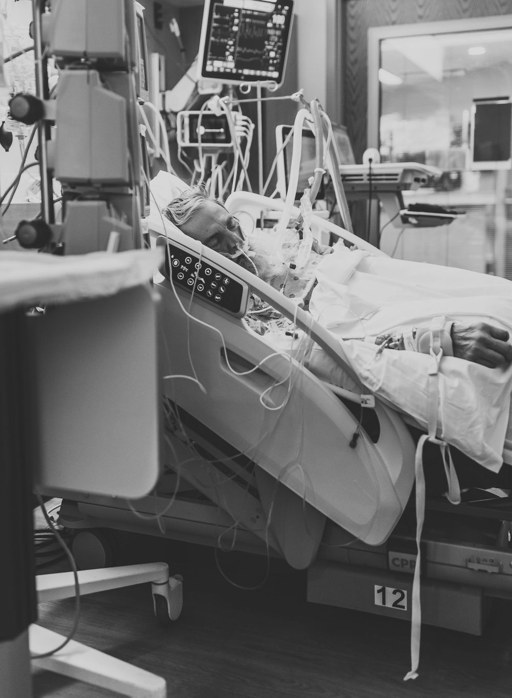 Black and white photograph of hospital beds with medical equipment and monitors in an intensive care unit.