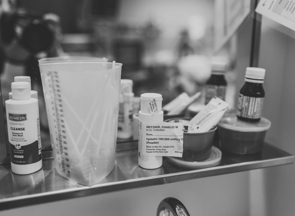 Black and white image of prescription medicine bottles and medical supplies arranged on a glass shelf.
