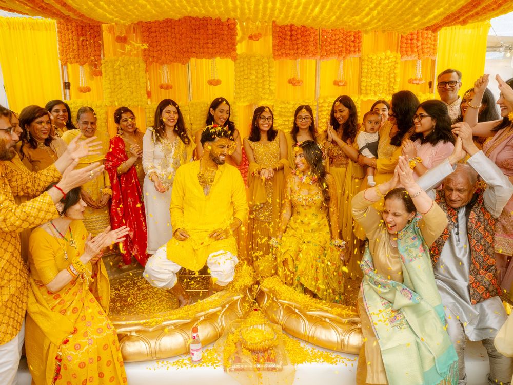 Guests celebrate at a vibrant yellow-themed haldi ceremony with traditional turmeric application rituals.