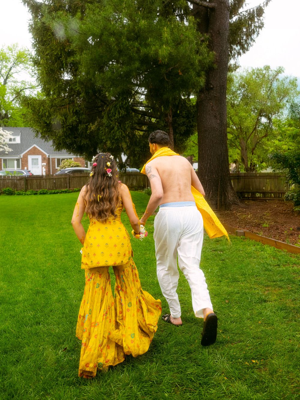 A couple walks through a lush green garden, with the person in a flowing yellow dress walking behind.