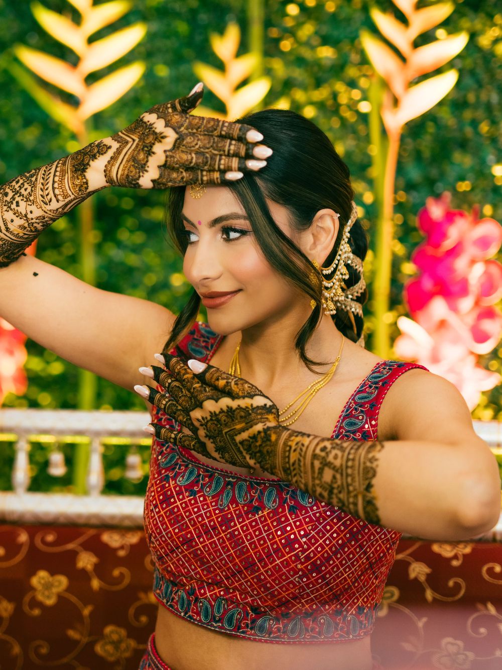 Close-up of intricate henna designs on hands with a red and blue embellished dress in the background.