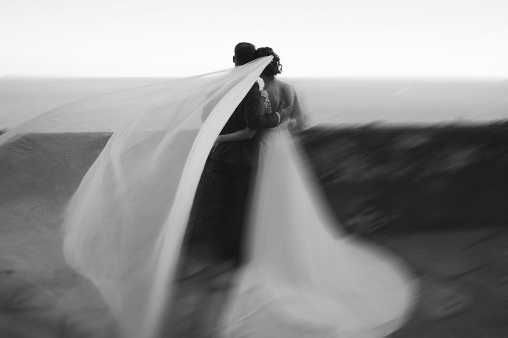 una foto artistica con gli sposi che guardano il mare e il velo che vola
