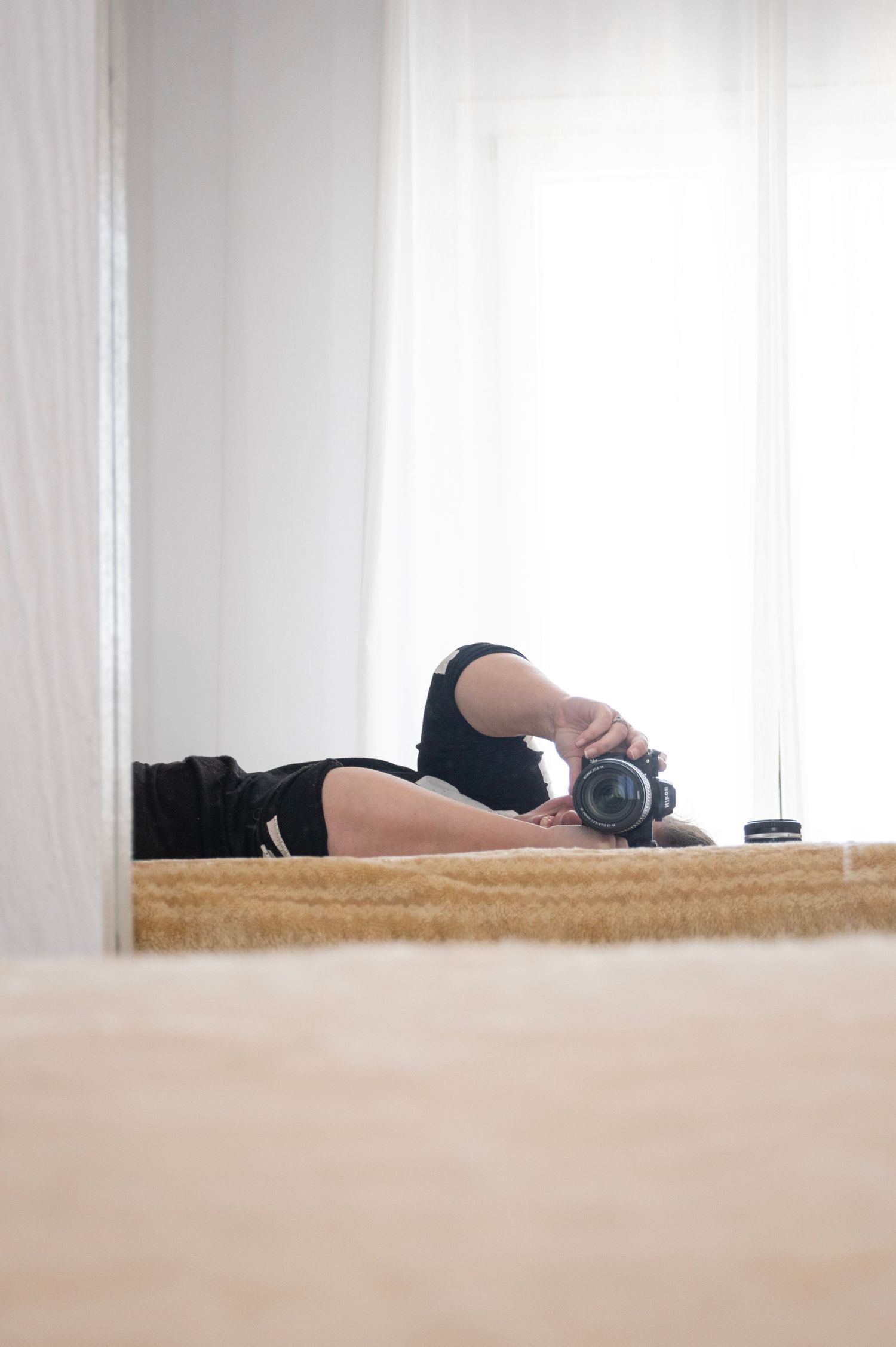 A camera lens peeks over the edge of a wooden surface in a minimalist composition.