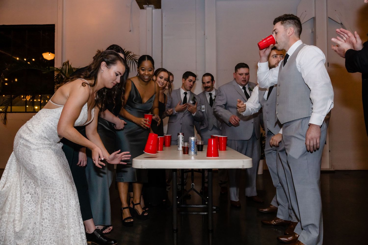A bride and groom share a fun dance moment with their wedding party on the dance floor at an evening reception.