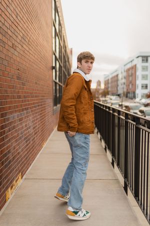 A high schooler in a tan jacket and jeans stands at one end of a brick-lined walkway, shown in a series of angles for his senior photos