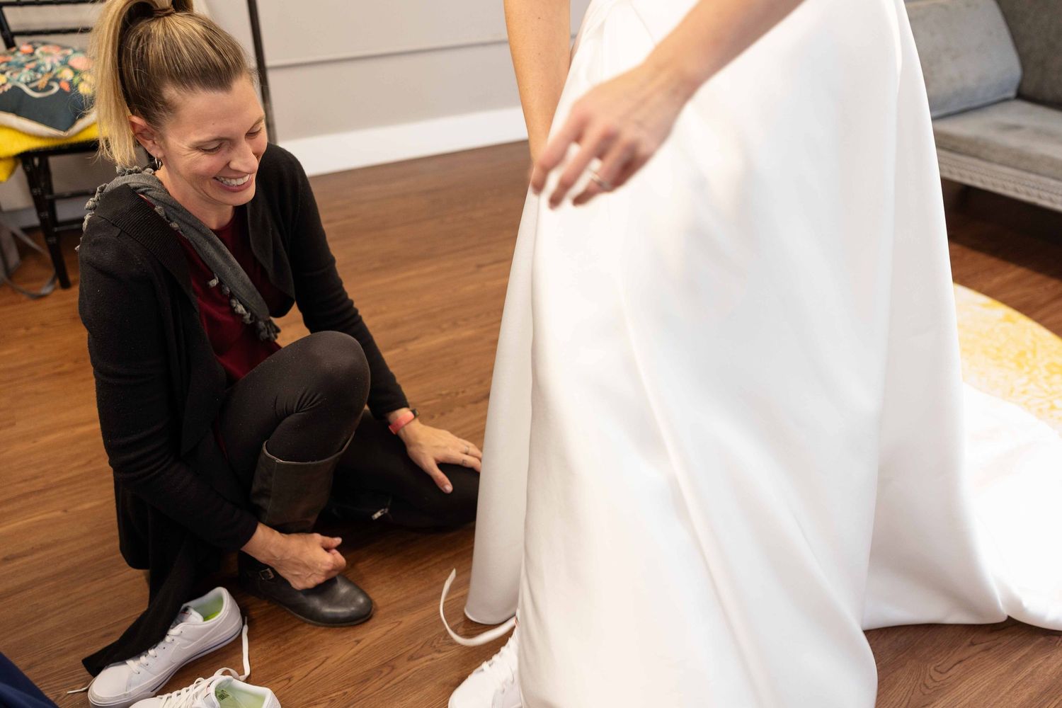A group of people gather around a white dress during a wedding dress fitting session.