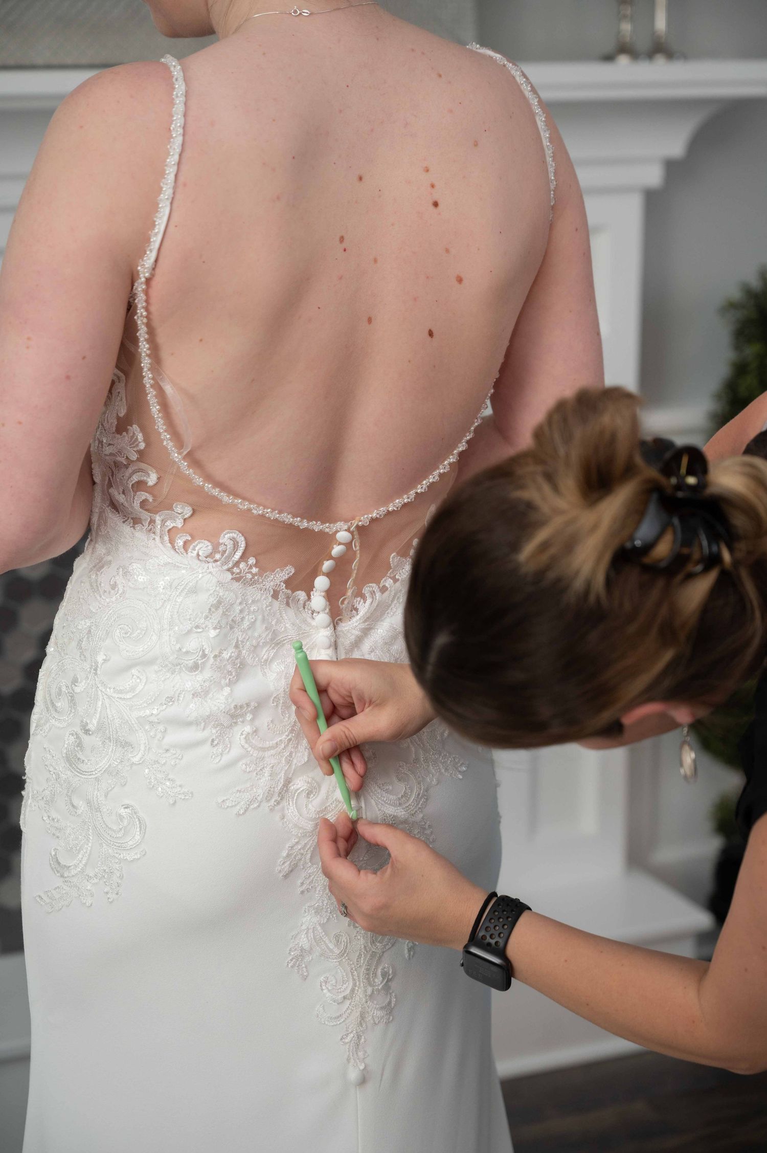 Someone helps adjust the delicate lace and beading details on the back of an elegant white wedding dress.