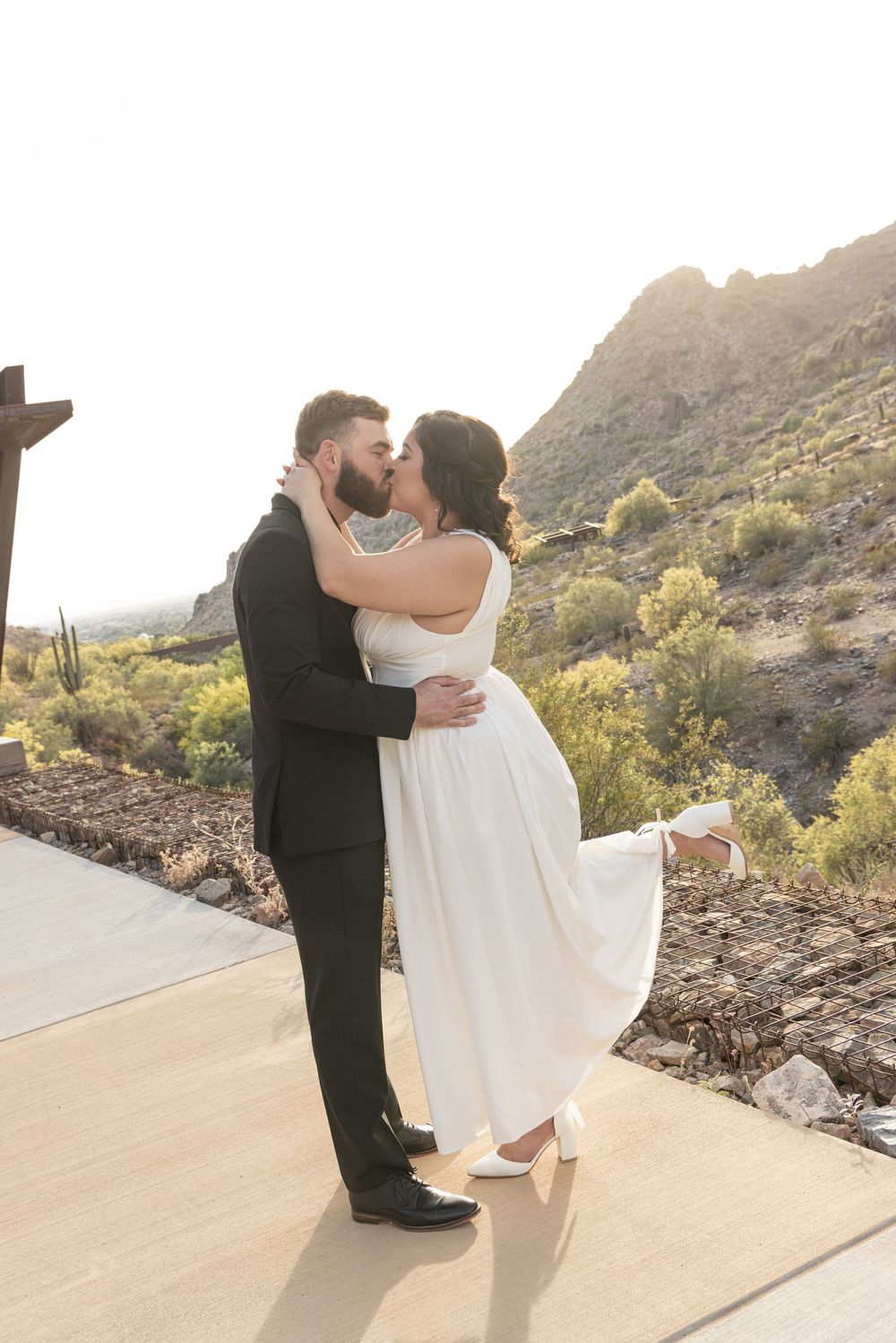 A couple in formal wedding attire share an intimate moment during their desert mountain photo session at sunset.