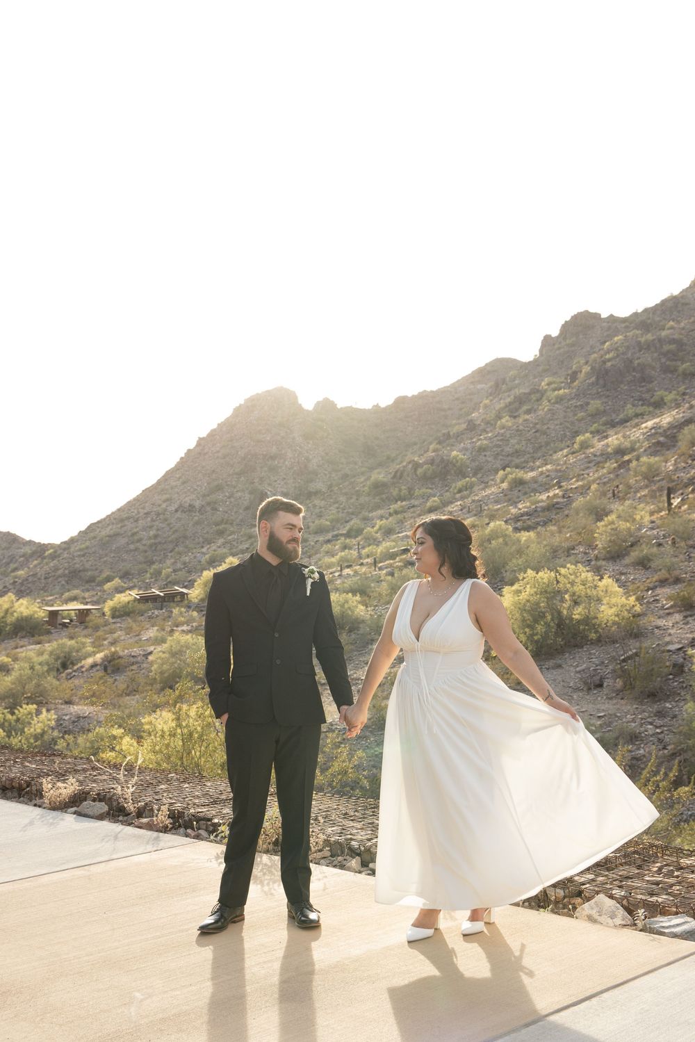 A couple in wedding attire dance together on a scenic mountain path during sunset.