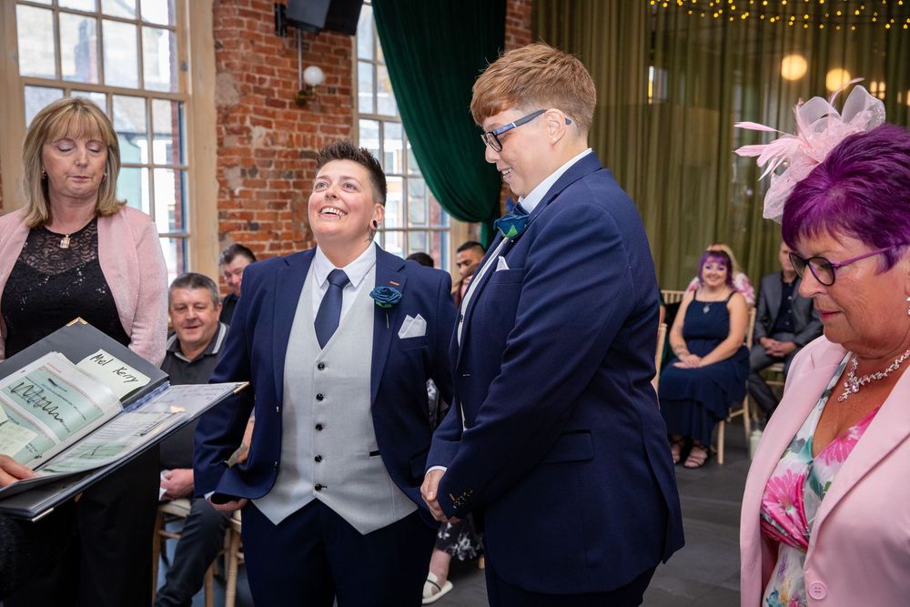 Two grooms share a joyful moment during their wedding ceremony while an officiant holds the marriage certificate.
