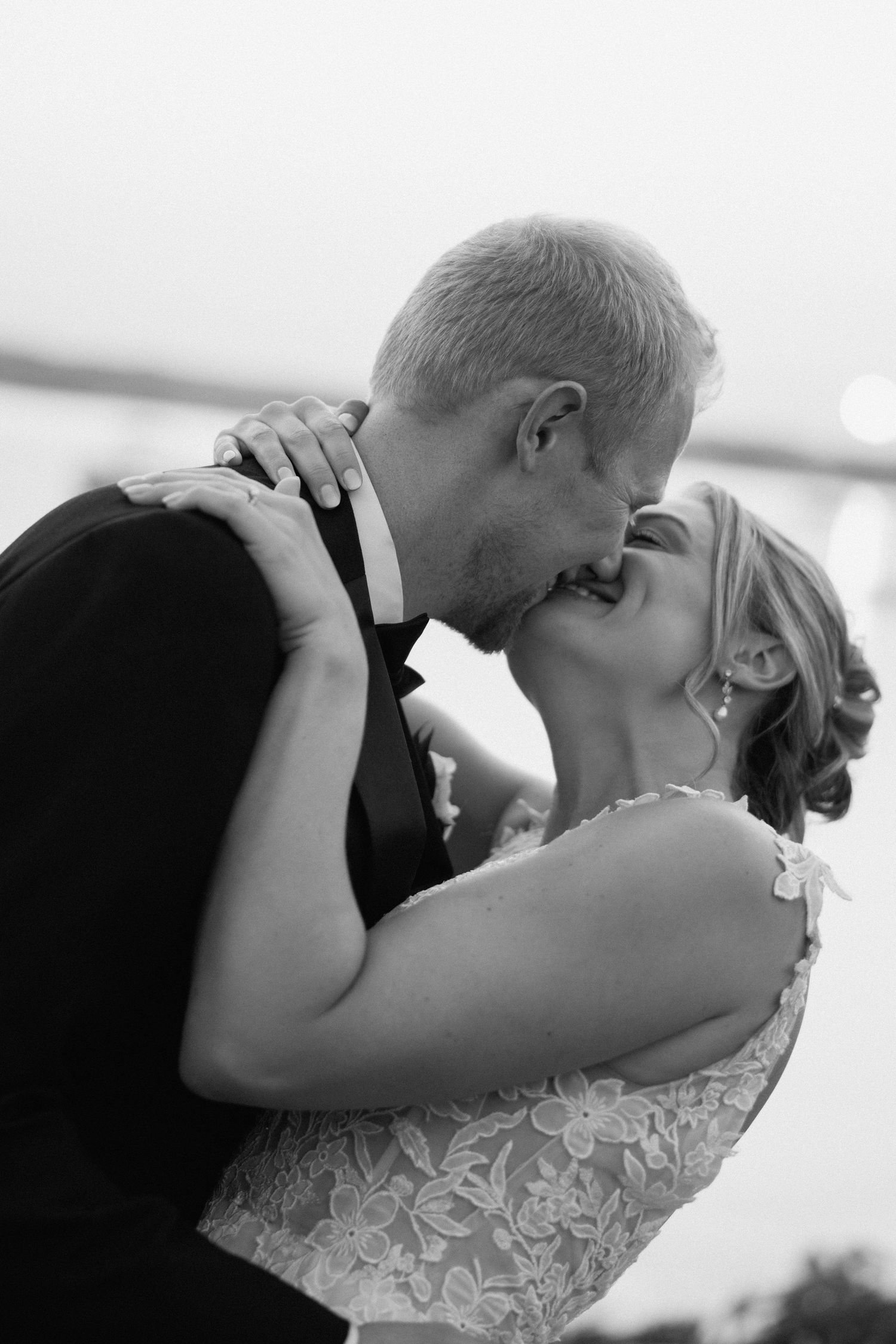 A romantic black and white wedding photo captures a tender kiss between newlyweds, with the bride in a lace dress.