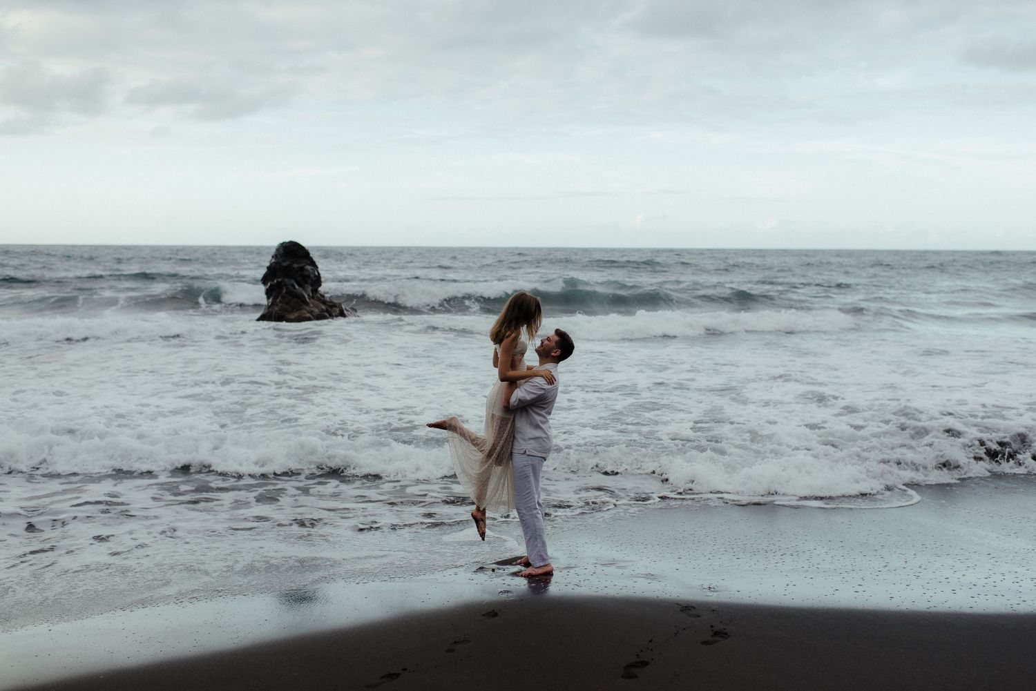 Romantic couple sharing a tender moment outdoors, woman smiling as man leans in close, with rocky background.