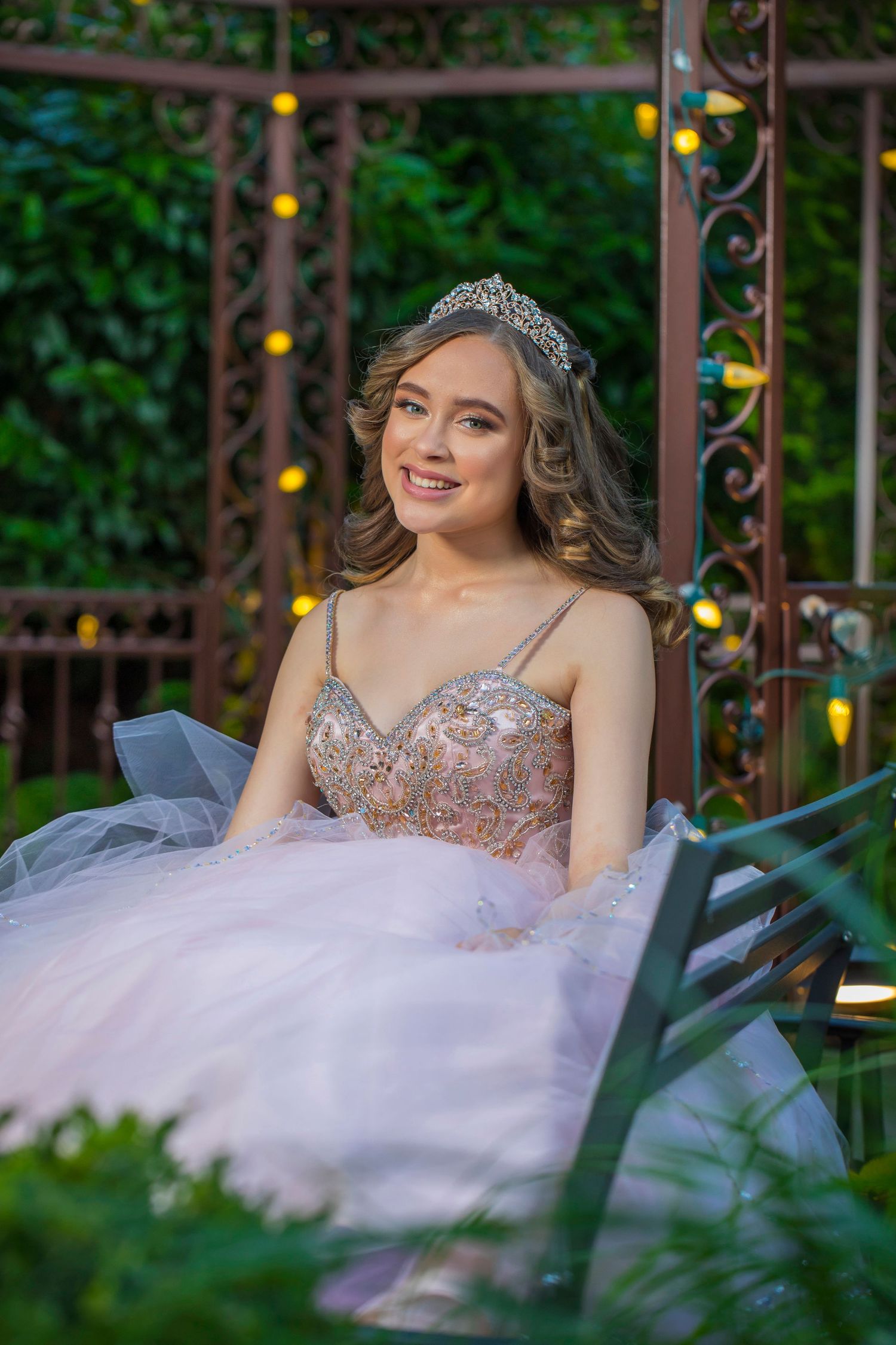 Elegant evening photoshoot in a garden gazebo with twinkling lights and lush greenery.