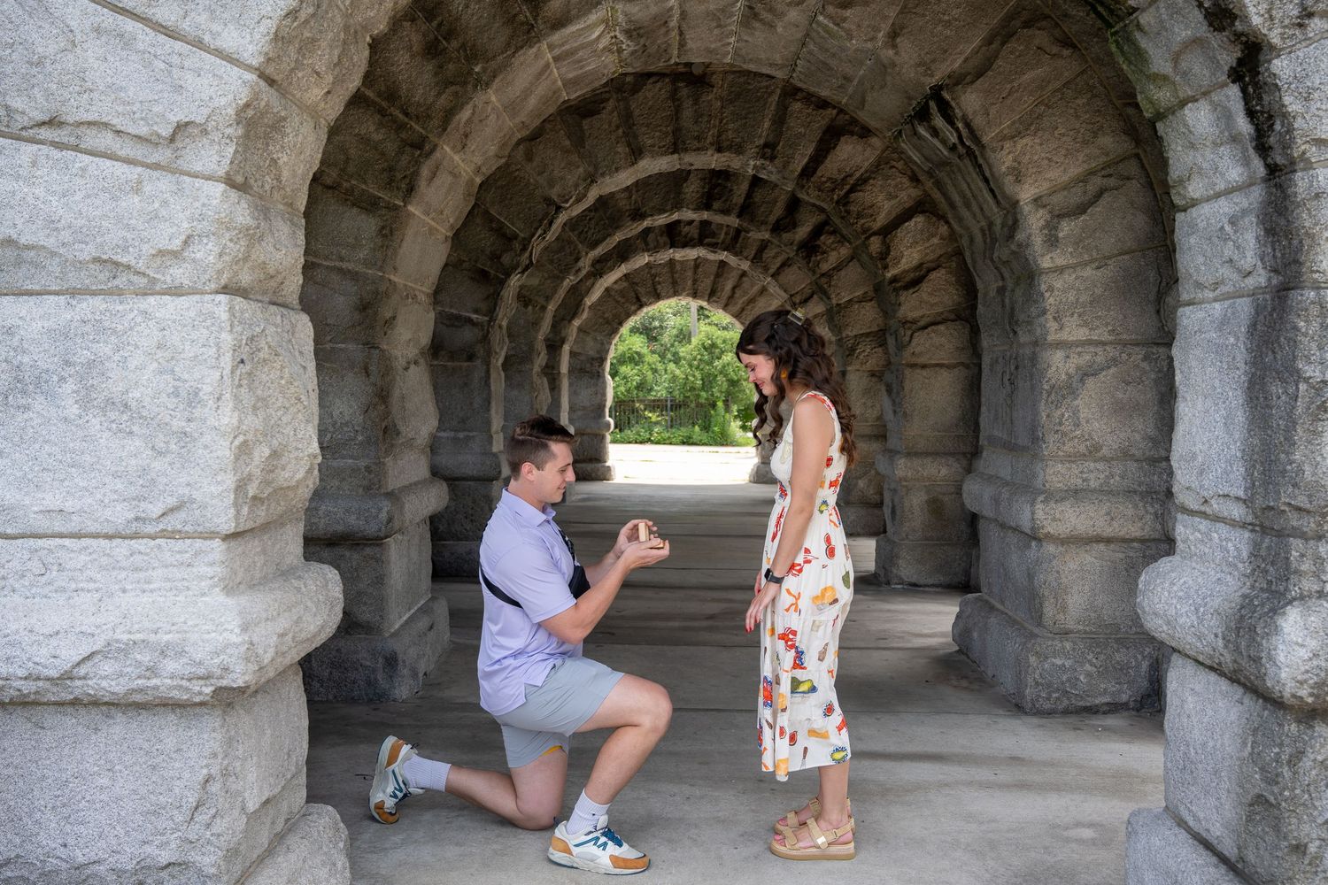 A romantic proposal moment captured in a stone archway tunnel with natural lighting.