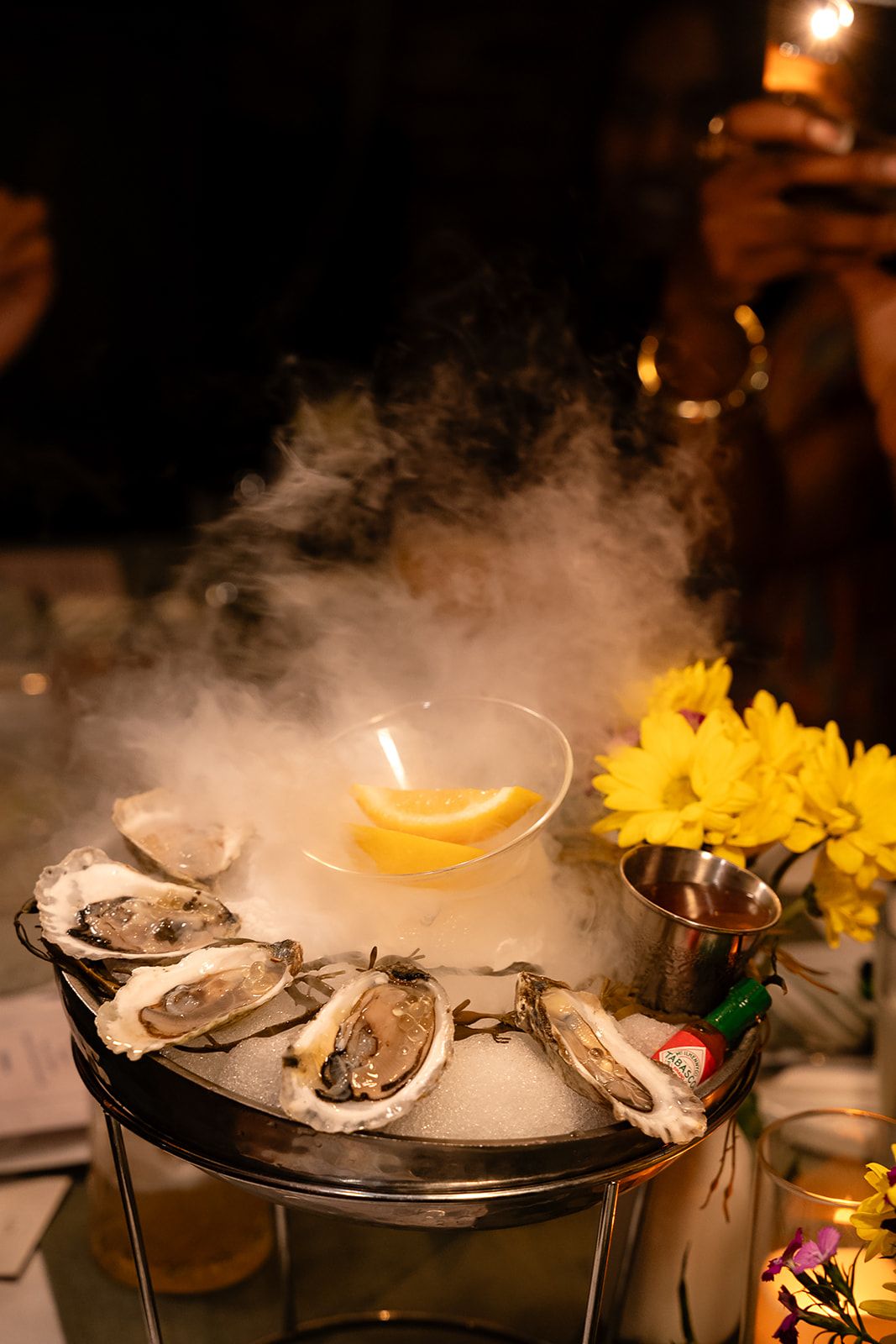 Fresh oysters on ice with dry ice smoke effect and lemon slices at an upscale dinner event.