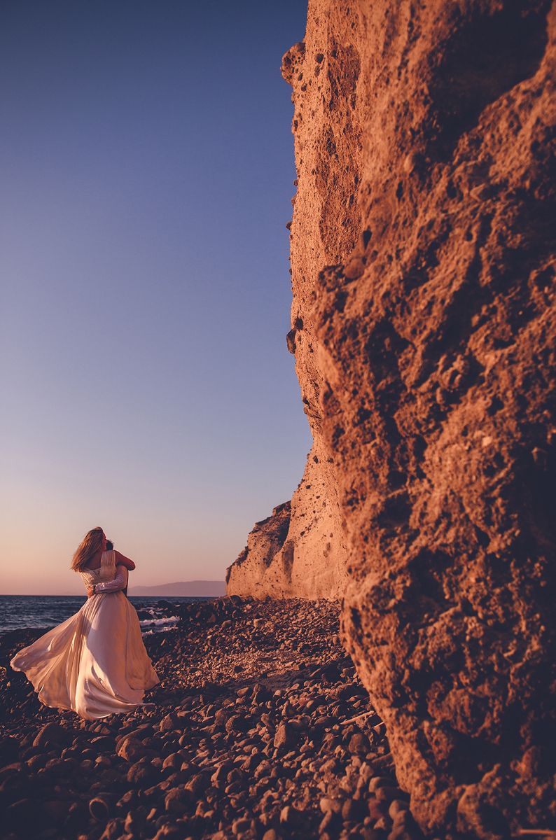 Couple walking along volcanic cliffs in Santorini at sunset by the sea