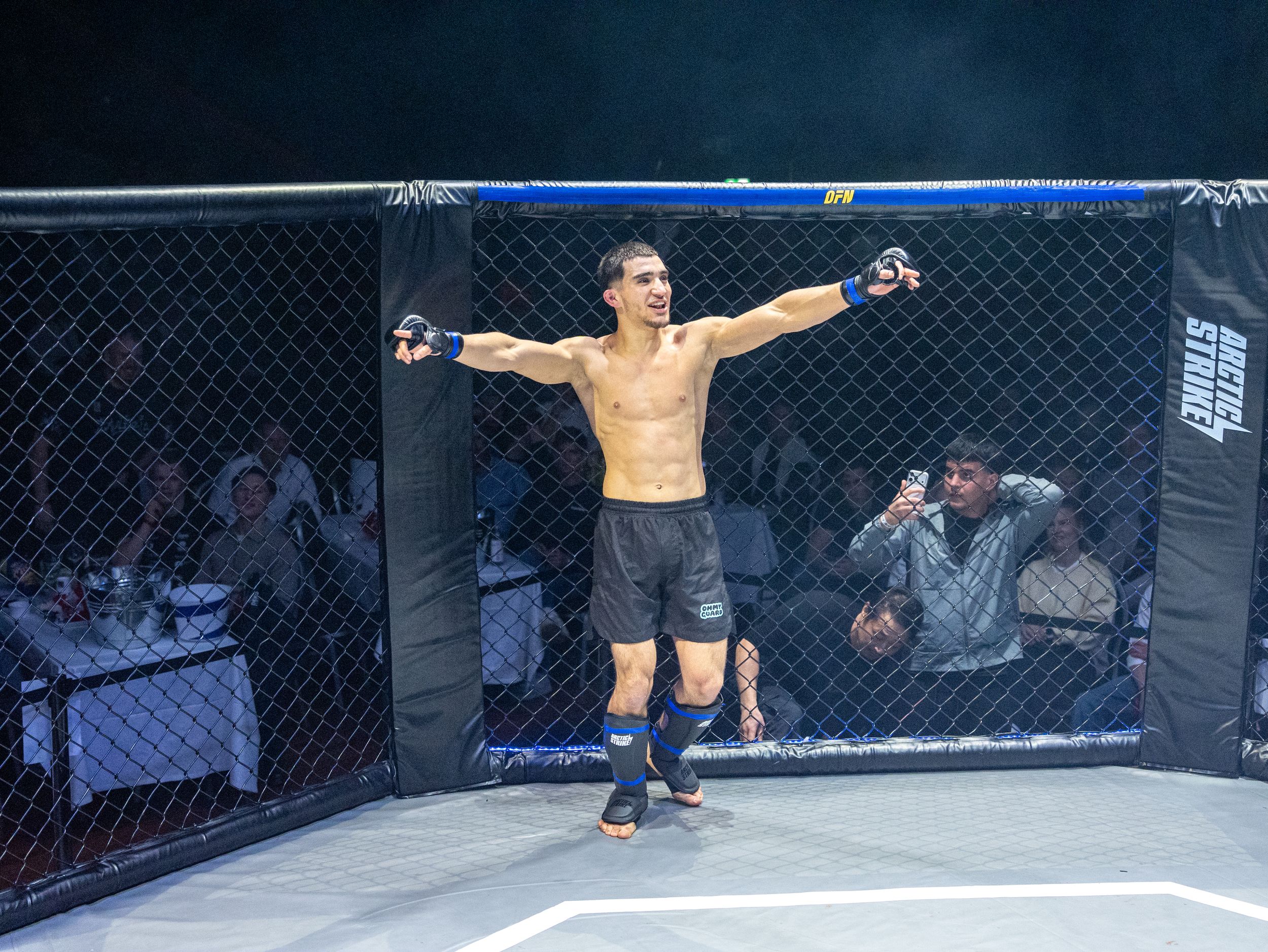 MMA fighter celebrates victory with arms raised in octagon cage during professional fight event.