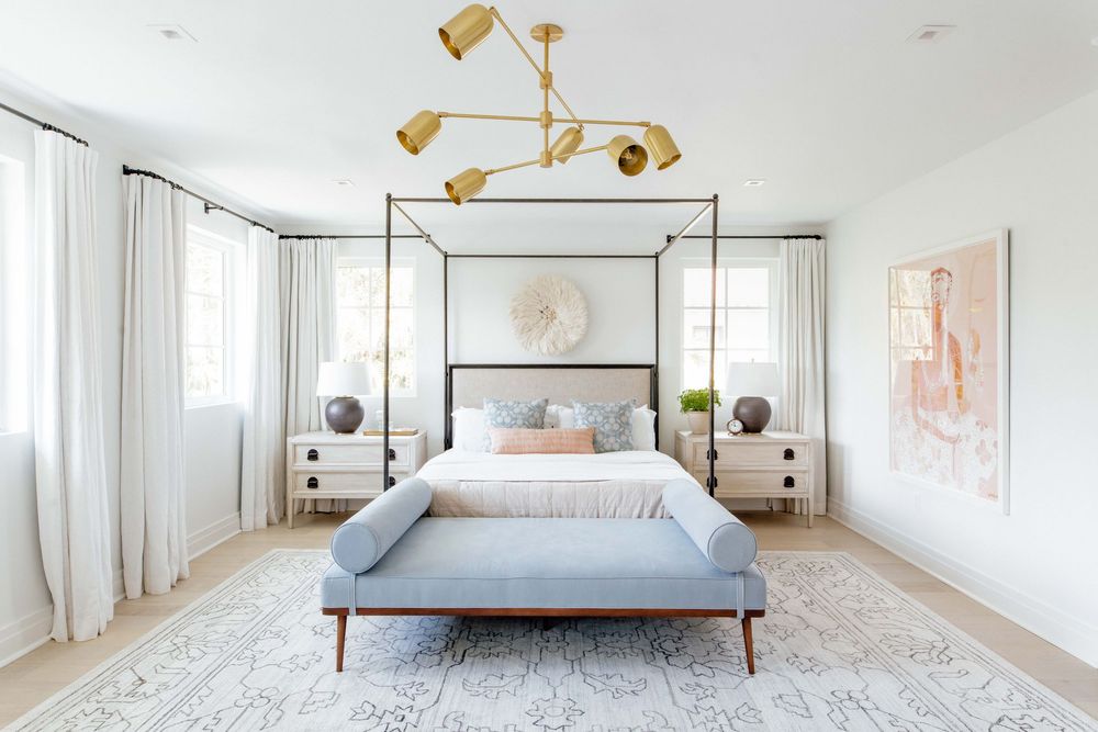 Elegant master bedroom with gold canopy bed, brass chandelier, blue bench, and neutral tones.