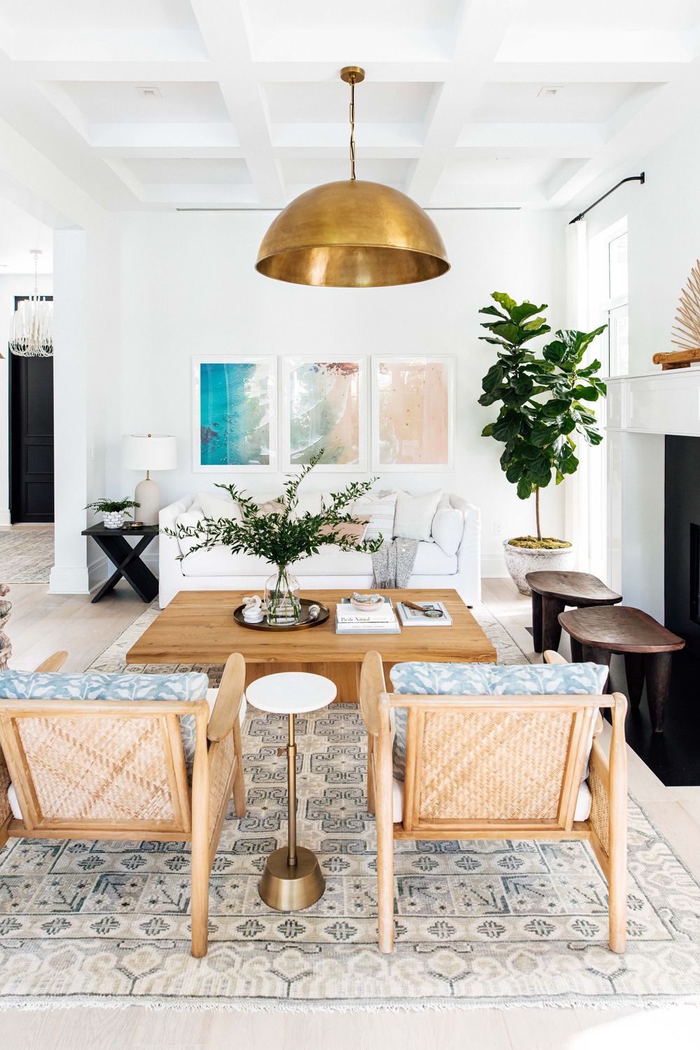 Bright living room with gold dome pendant, rattan chairs, wood coffee table, white sofas, and colorful abstract art gallery wall.