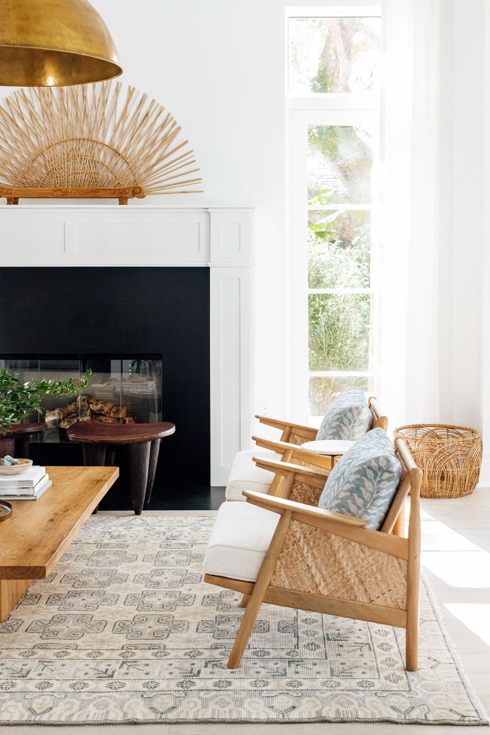 Minimalist living room with gold pendant light, wood rattan chairs, black fireplace, and neutral patterned area rug.