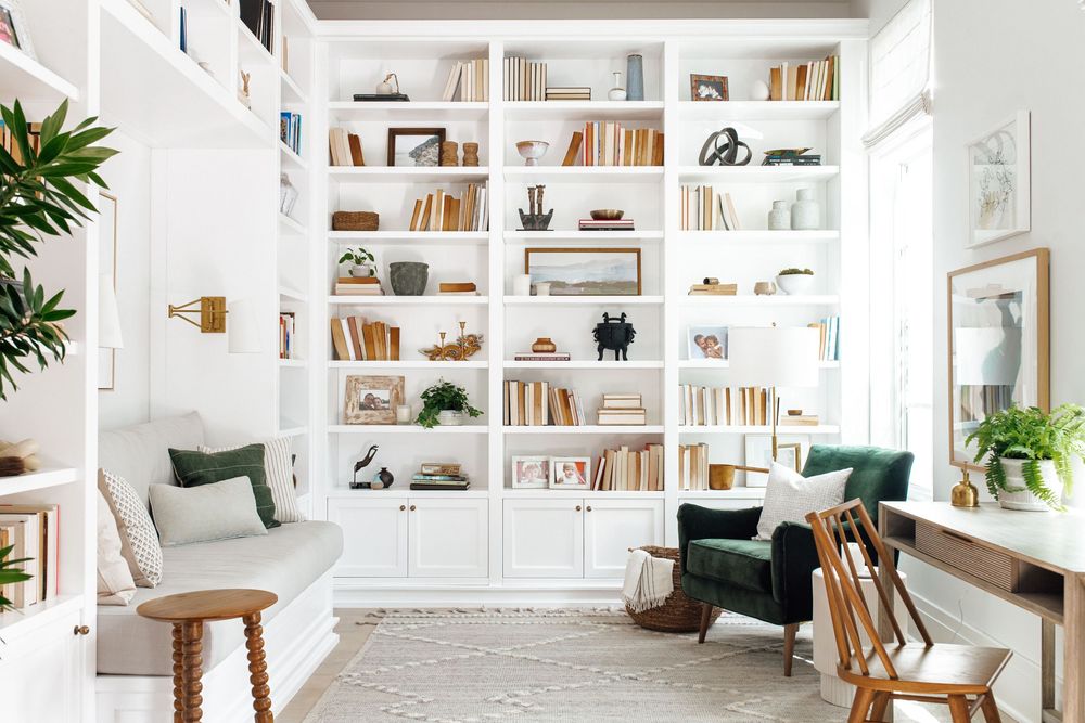 Bright home office with floor-to-ceiling white built-in bookshelves and green velvet chairs.