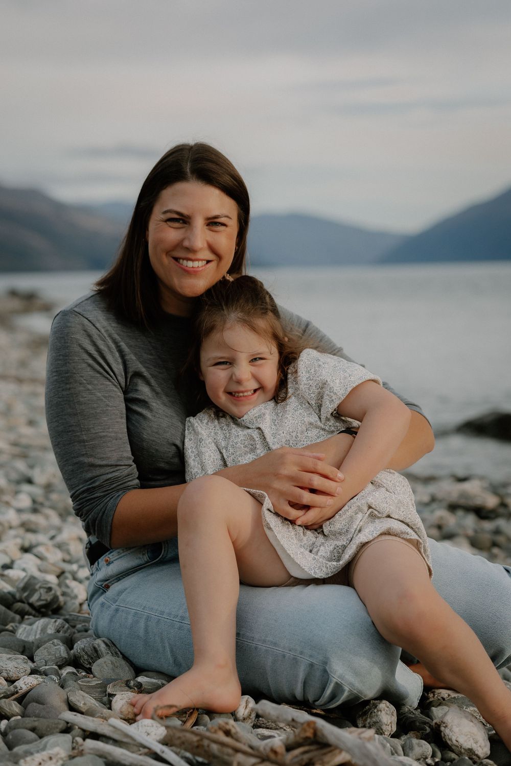 A smiling mother hugs her young daughter at Lake Wakatipu, Homestead Bay in Queenstown during a family photoshoot.