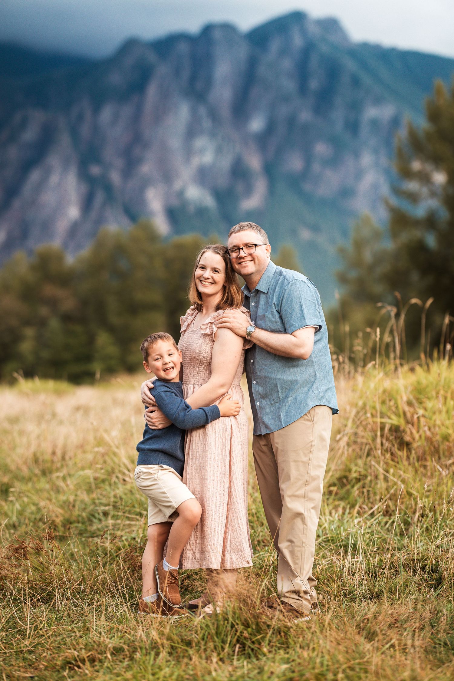 Family lying on blanket in grass with mountain landscape and golden autumn colors in background.