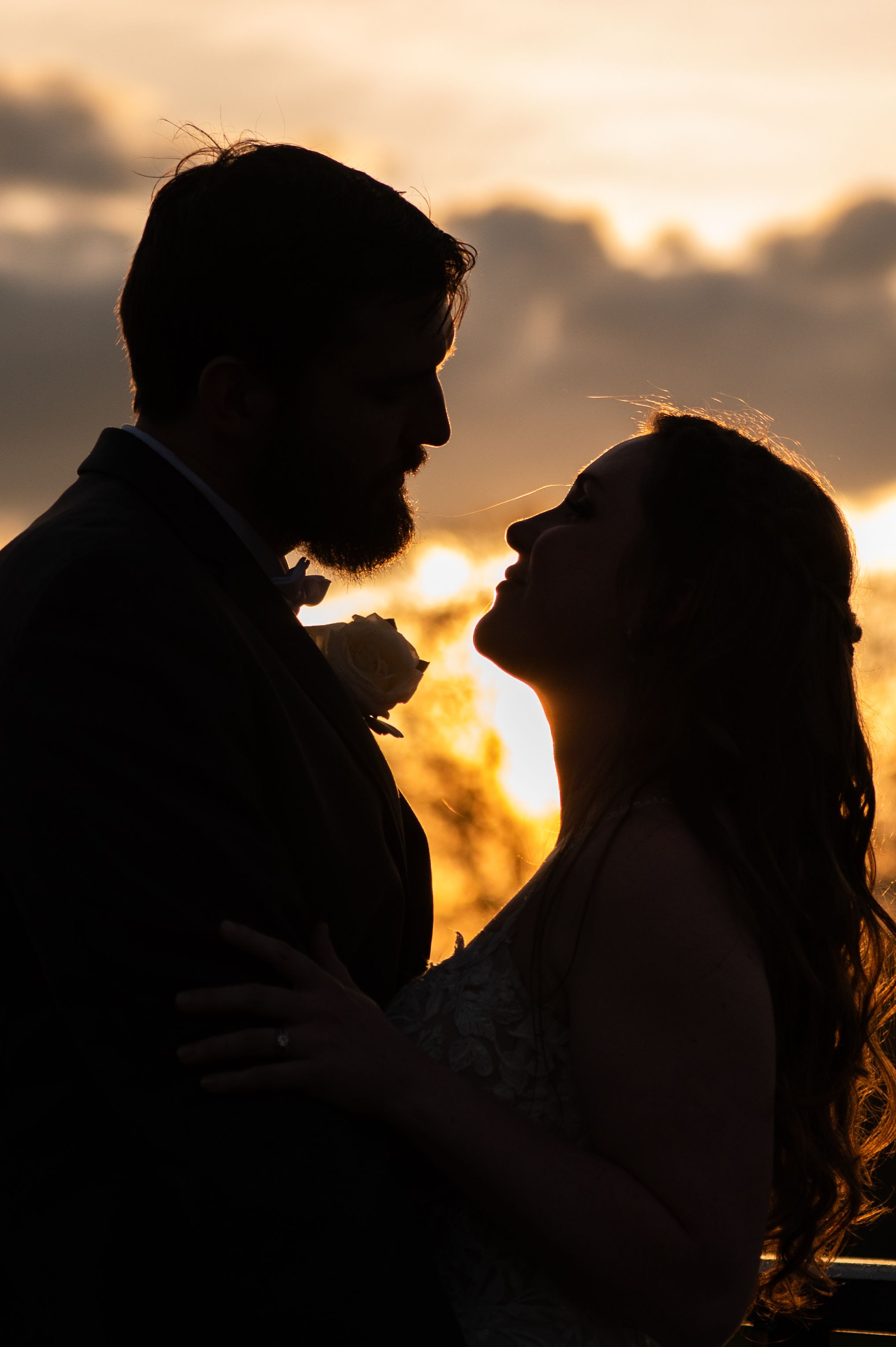 Silhouette of a couple in a romantic embrace against a dramatic sunset sky with golden clouds.