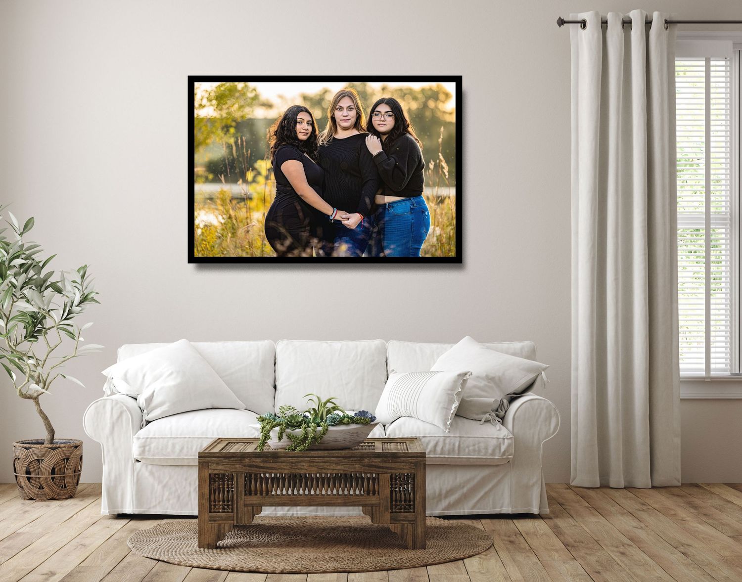 Framed portrait of three women in black outfits displayed above a white couch in a bright living room.