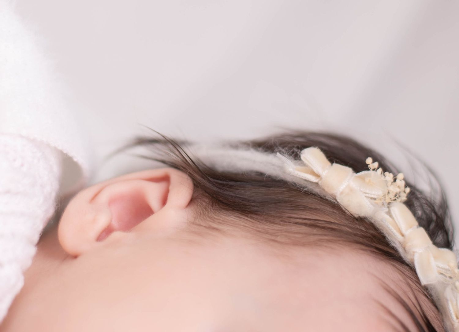 Close-up of sleeping newborn baby with dark hair wearing a delicate floral headband.