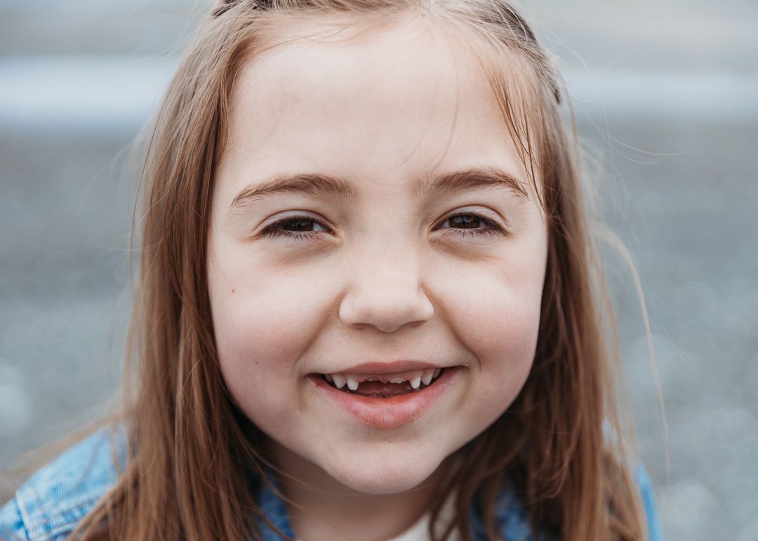 A smiling child with brown hair shows a missing tooth while looking at the camera.